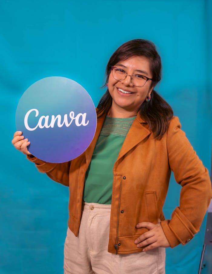 gallery-5 A smiling woman in a casual outfit holds a Canva sign, posing confidently against a vibrant blue backdrop.